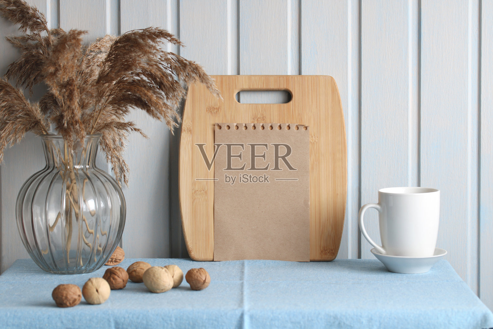 空白笔记本模型，配有切菜板、芦苇草和胡桃，放在蓝色桌布上。乡村风格的模型。照片摄影图片