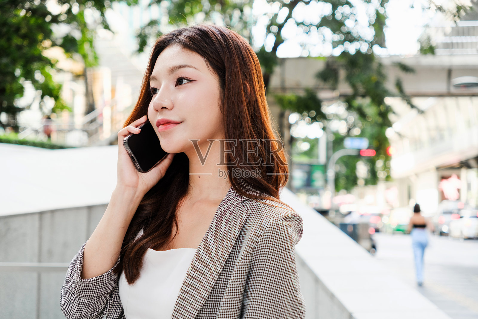 一位年轻的亚洲女商人在户外穿着时尚的服装，正在打电话，背景是繁忙的城市景象。年轻女商人的主角。照片摄影图片