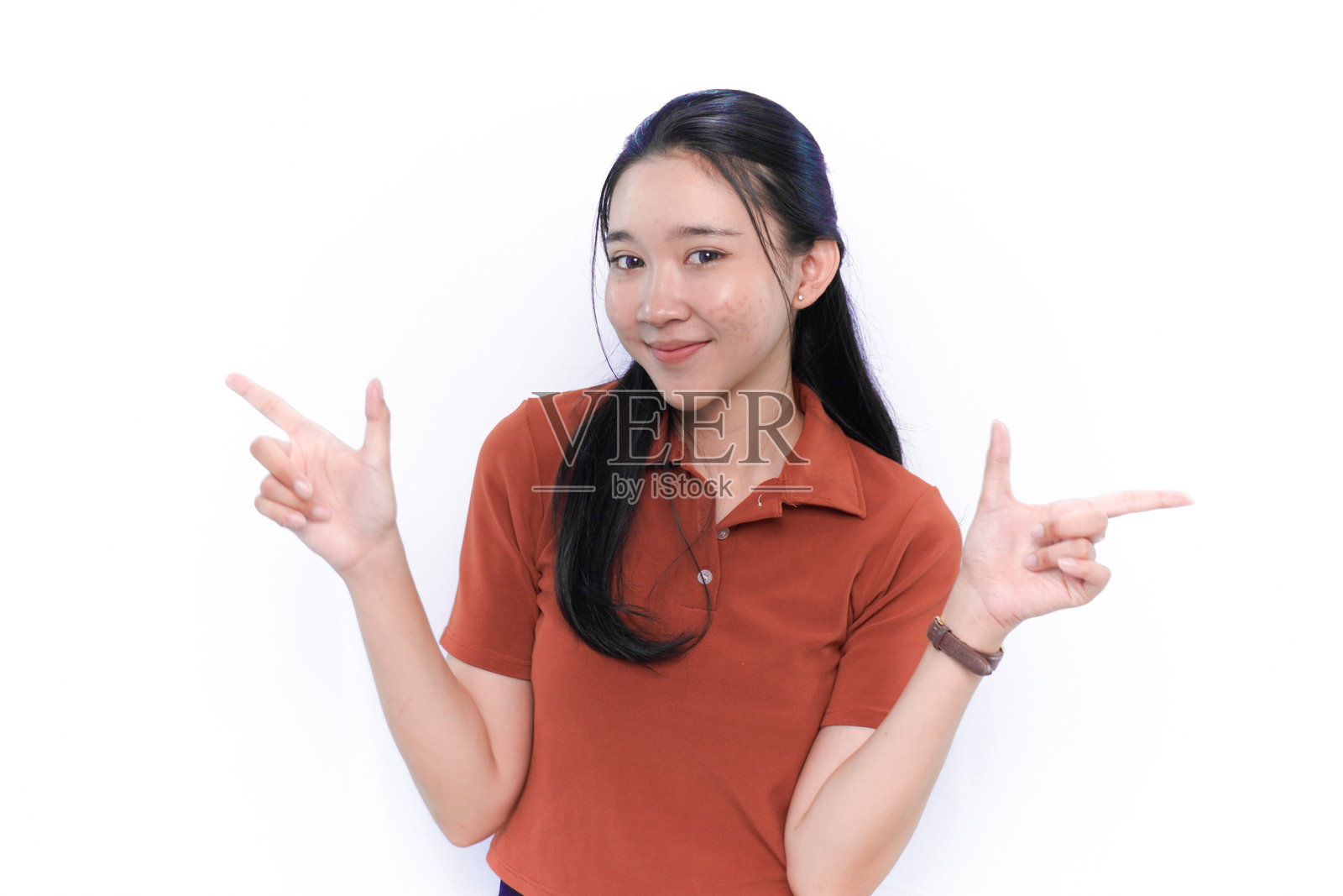 微笑并指向一侧的亚洲印尼模特，穿着橙色衣服。照片摄影图片