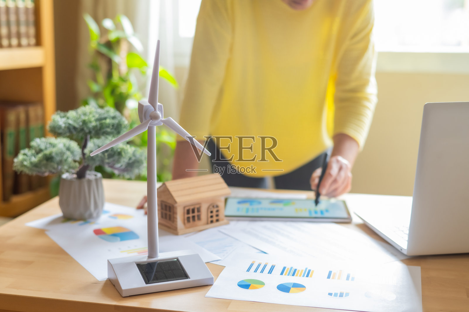 工程师在数字平板上处理图表和图形。评估可再生能源解决方案在可持续房屋模型中的效率。展示了一个微型风力涡轮机和太阳能电池板。照片摄影图片
