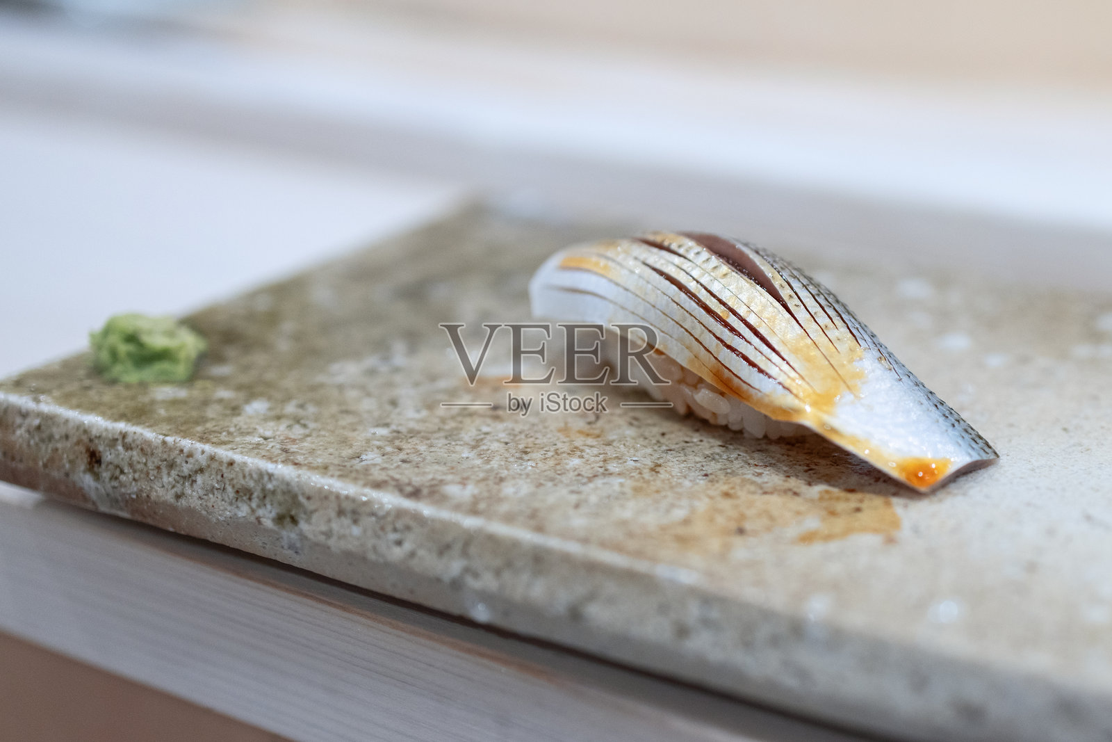 精致的刀工切割的肠鳗寿司，光滑的质感，摆放在石板上，旁边有芥末，突显出精细的工艺和传统的制作方式。照片摄影图片