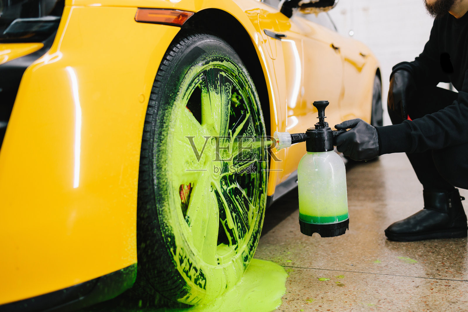 清洁工在洗车场用刷子和清洁剂用绿色泡沫清洗汽车轮胎。汽车护理的细节处理程序。照片摄影图片