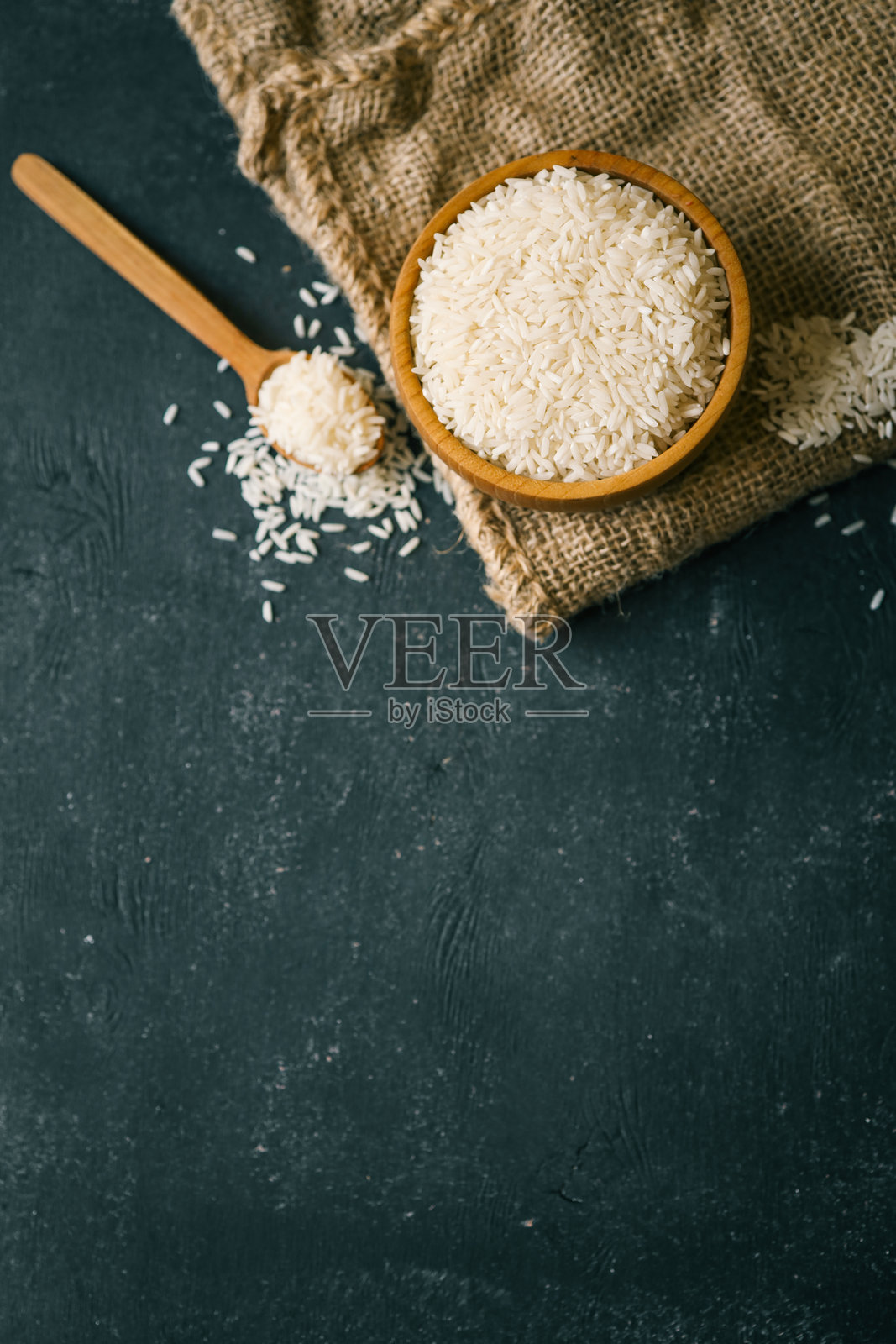 从上方看原料白米，放在木碗中，旁边有勺子和麻布袋，背景为深色纹理。乡村风格的厨房布置，搭配自然食材。照片摄影图片