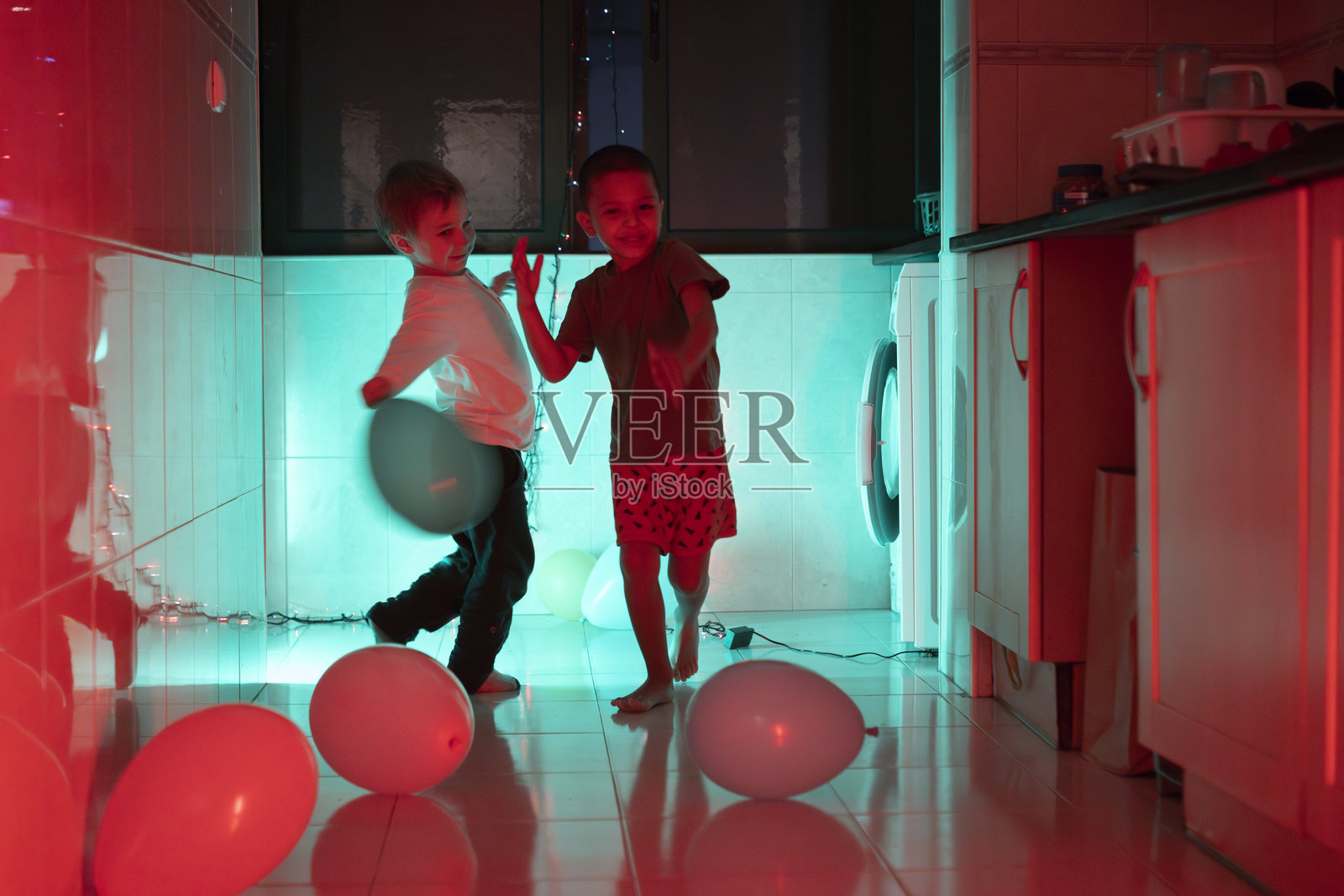 两个兄弟在厨房里玩气球，周围有红色和青色的灯光。照片摄影图片