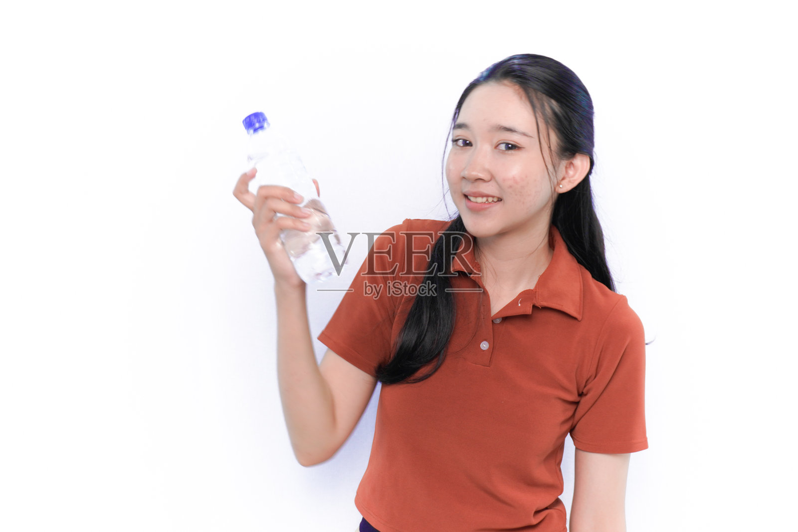 微笑的亚洲印尼模特穿着橙色连衣裙，手里拿着一瓶饮料。照片摄影图片