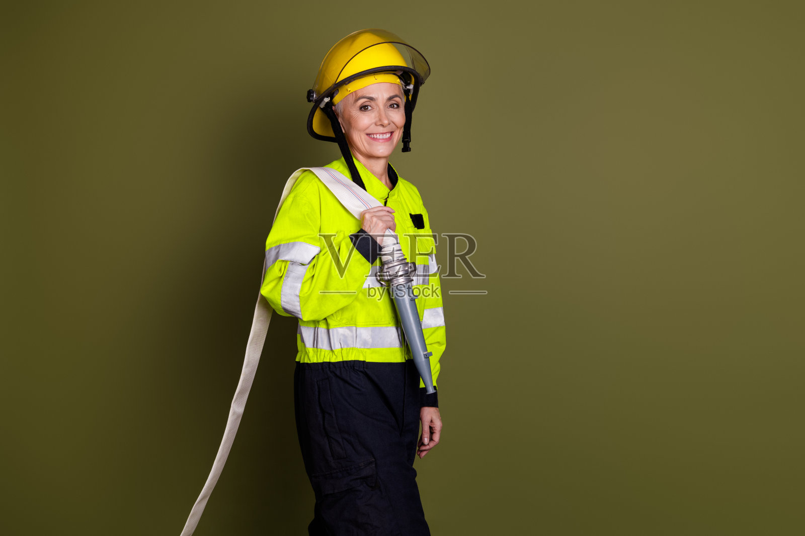 自信的女性消防员穿着制服，准备在卡其色背景下行动。中年女性展现出力量。照片摄影图片