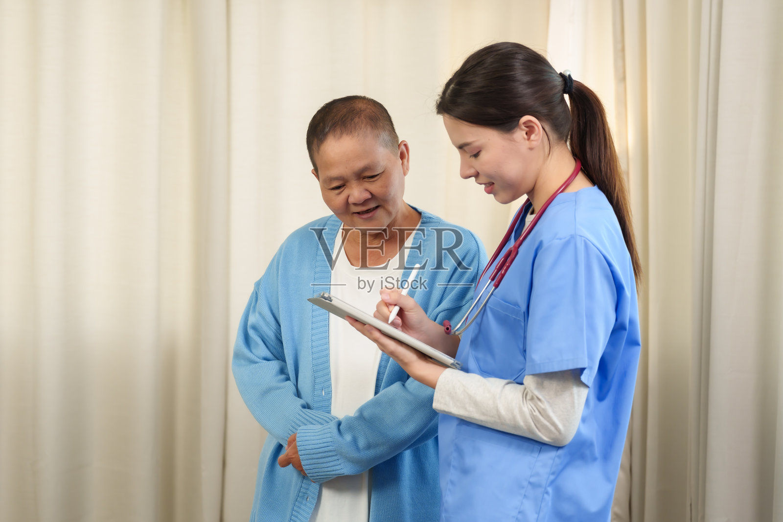 物理治疗师在病人康复后照顾老人。穿着蓝色制服的微笑年轻护士向老人展示平板电脑上的健康信息。家庭医疗技术的应用。照片摄影图片