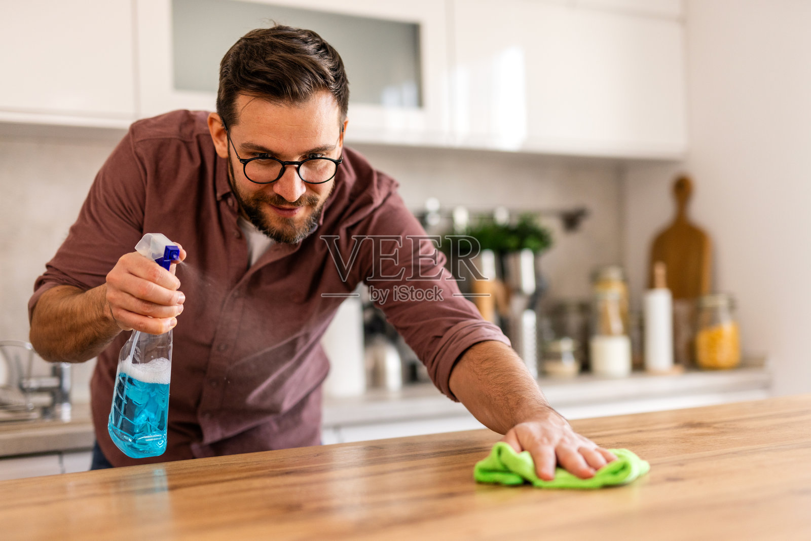 一个男人在家里清洁桌子，擦拭表面以保持空间的整洁和有序。这张图片捕捉了一个温馨日常环境中家庭维护和关注清洁的瞬间。照片摄影图片