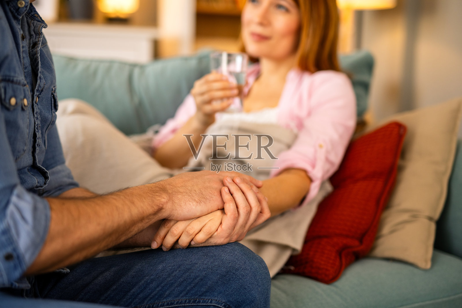 关心的男人轻轻地用温暖的毯子为生病的妻子盖上，她在沙发上休息。她看起来虚弱而不适，但他的陪伴和善良在他们温馨而充满爱的家中带来了安慰。照片摄影图片