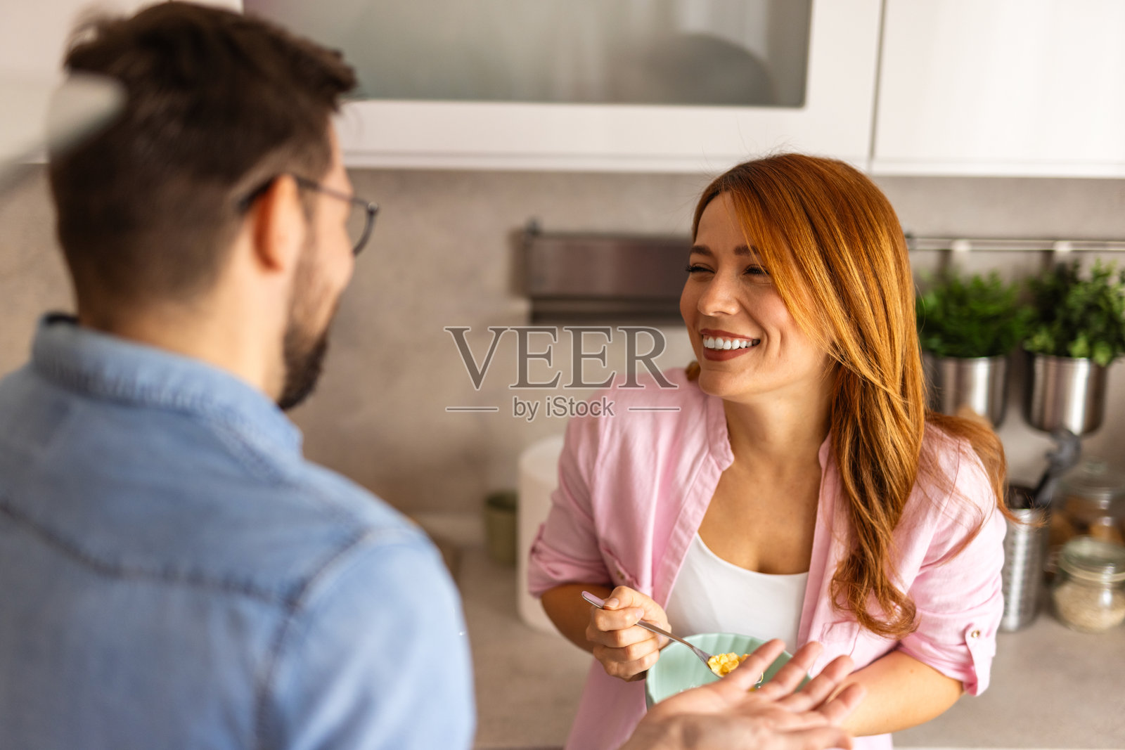 一对快乐的情侣在温馨的厨房里享用早餐，边准备麦片边欢笑。他们温暖而亲密的互动反映了坚固的关系和愉快的晨间习惯。照片摄影图片