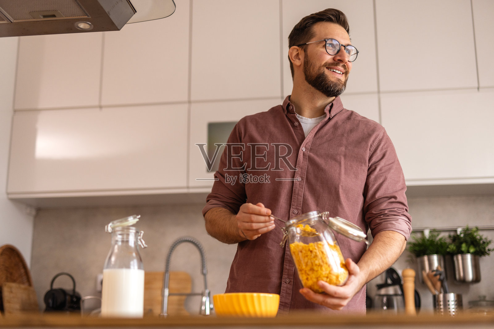 男人在厨房为早餐准备麦片，往麦片碗里倒牛奶。这是每天的早晨例行公事，唤起了舒适、滋养和简单的日常开始的感觉。照片摄影图片