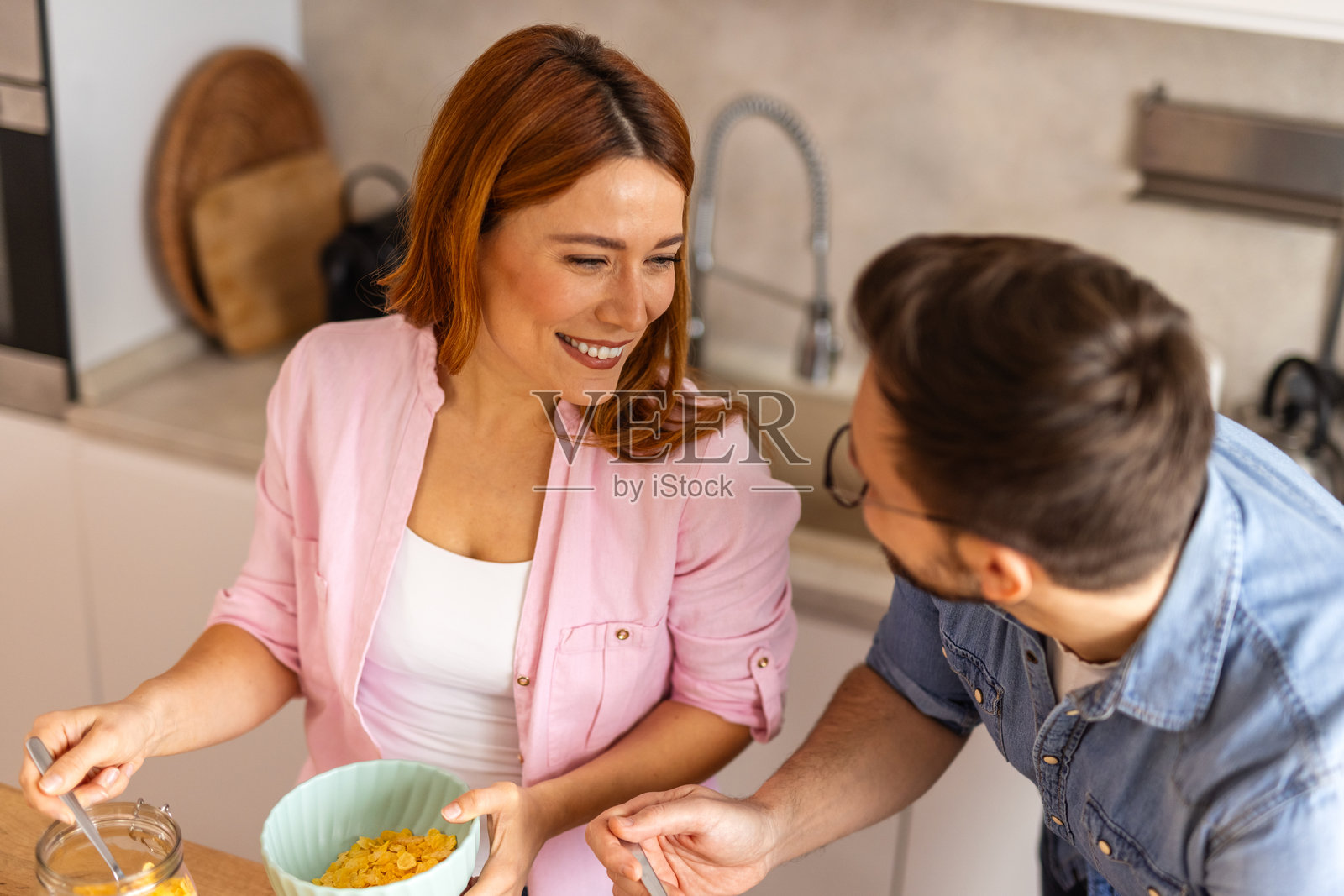 一对年轻情侣在自家厨房开始他们的早晨，享用自制的早餐，快乐地一起吃麦片和牛奶。他们欢笑着，分享温馨的时刻，营造出愉快的氛围。照片摄影图片