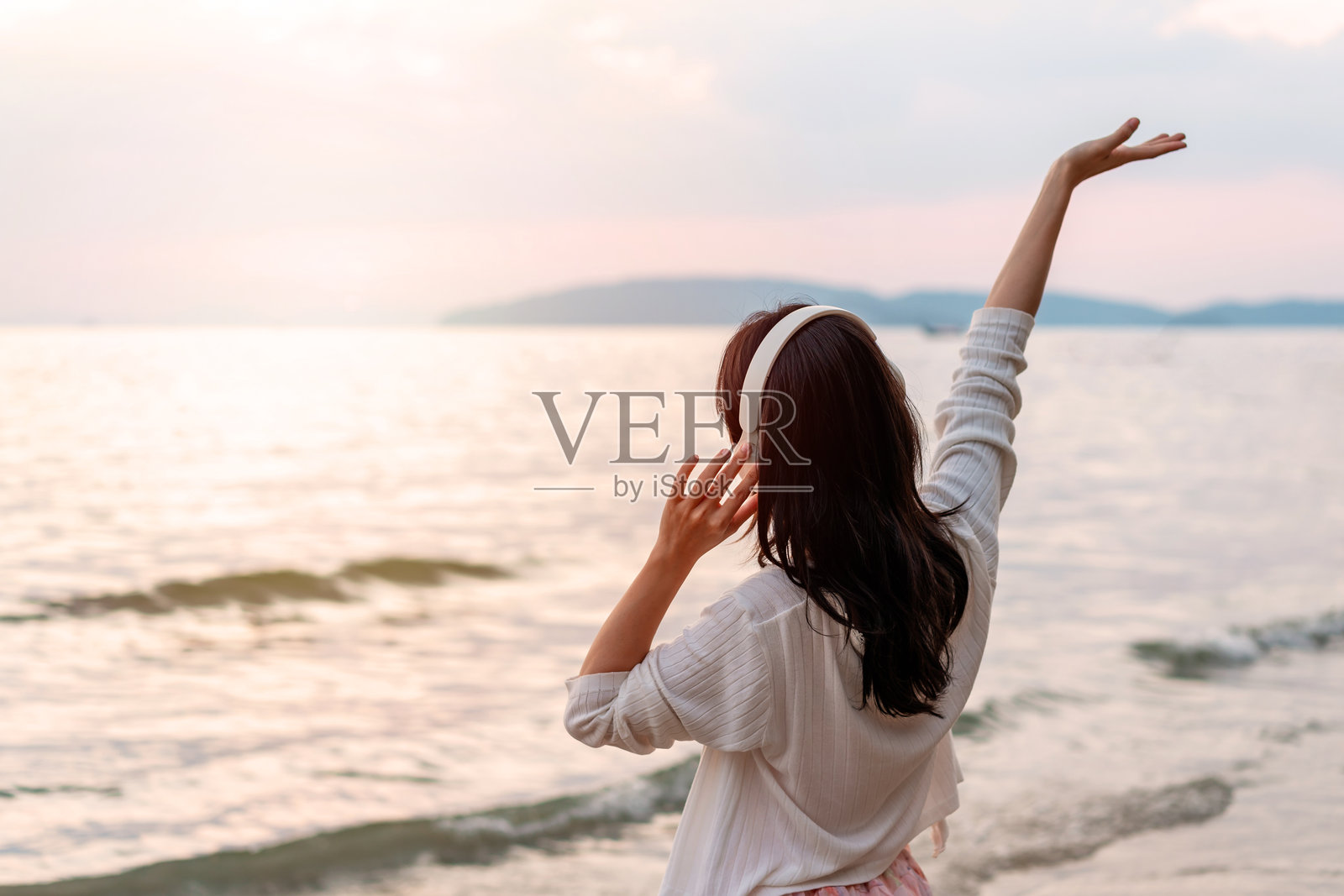 年轻快乐的亚洲女性在宁静的海滩上放松，享受美丽的日落和音乐。照片摄影图片