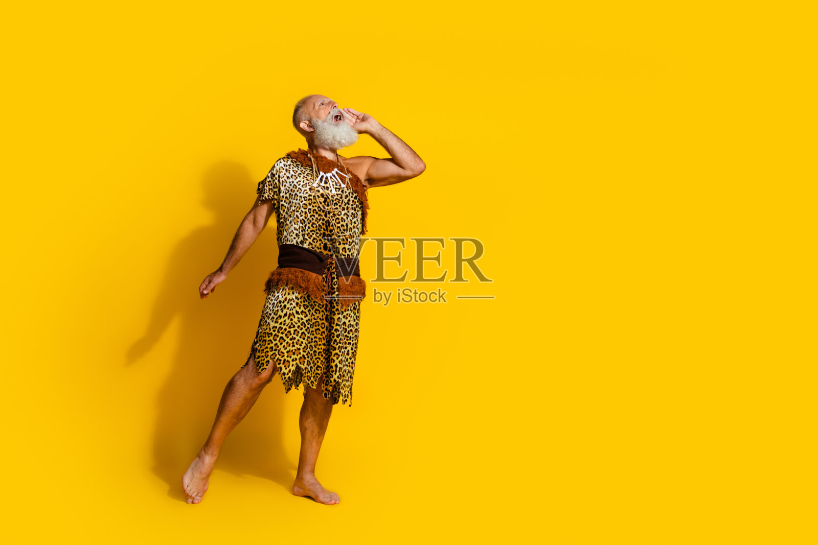 穿着豹纹毛皮的愤怒原始人全身照，正在大喊，背景为黄色，留有空白空间。照片摄影图片
