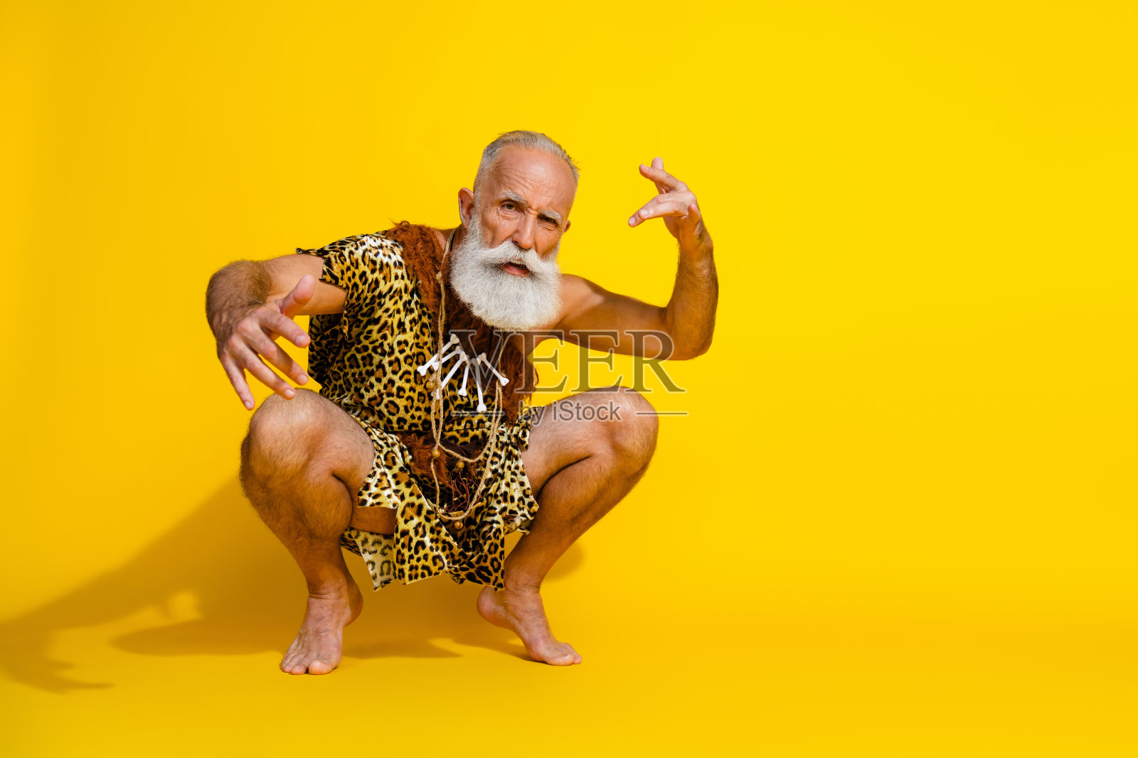 全身肖像原始穴居人赤脚坐在空旷的地方，穿着豹纹衣服，背景为黄色。照片摄影图片