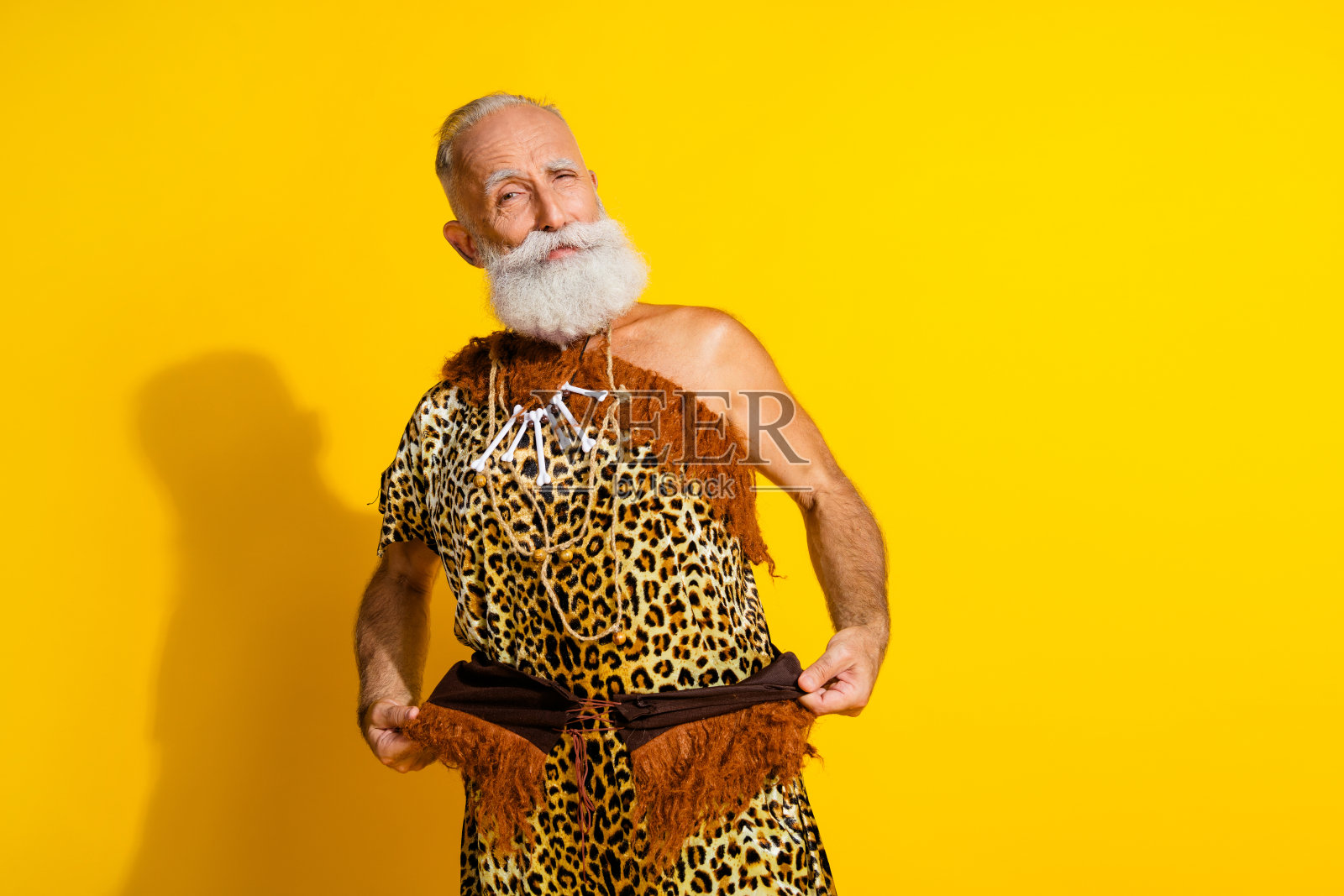 穿着豹纹毛皮的搞笑野蛮人展示服装，背景为黄色，留有空白空间。照片摄影图片
