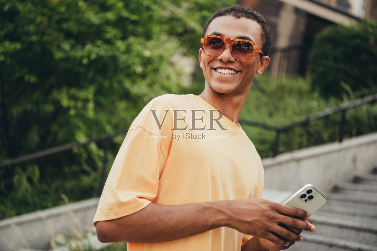 快乐的年轻人在城市环境中行走，戴着时尚的太阳镜和黄色T恤，享受阳光明媚的户外时光。照片摄影图片