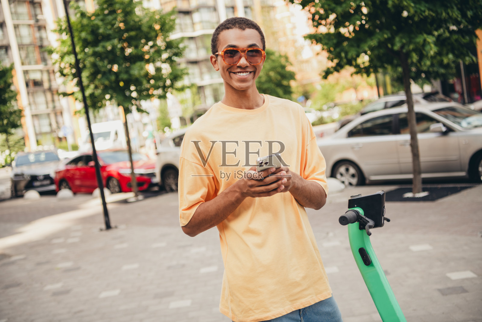 年轻男子穿着时尚T恤，微笑着在白天的城市街道上拿着智能手机。照片摄影图片