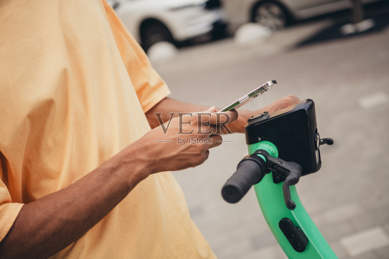 年轻男子穿着时尚休闲服装，在白天的城市街道上站在电动滑板车旁查看手机。照片摄影图片