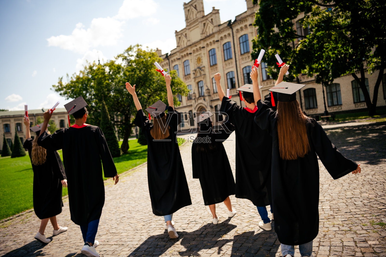 一群学生在户外大学建筑前举起文凭，戴着学位帽的背影照片照片摄影图片