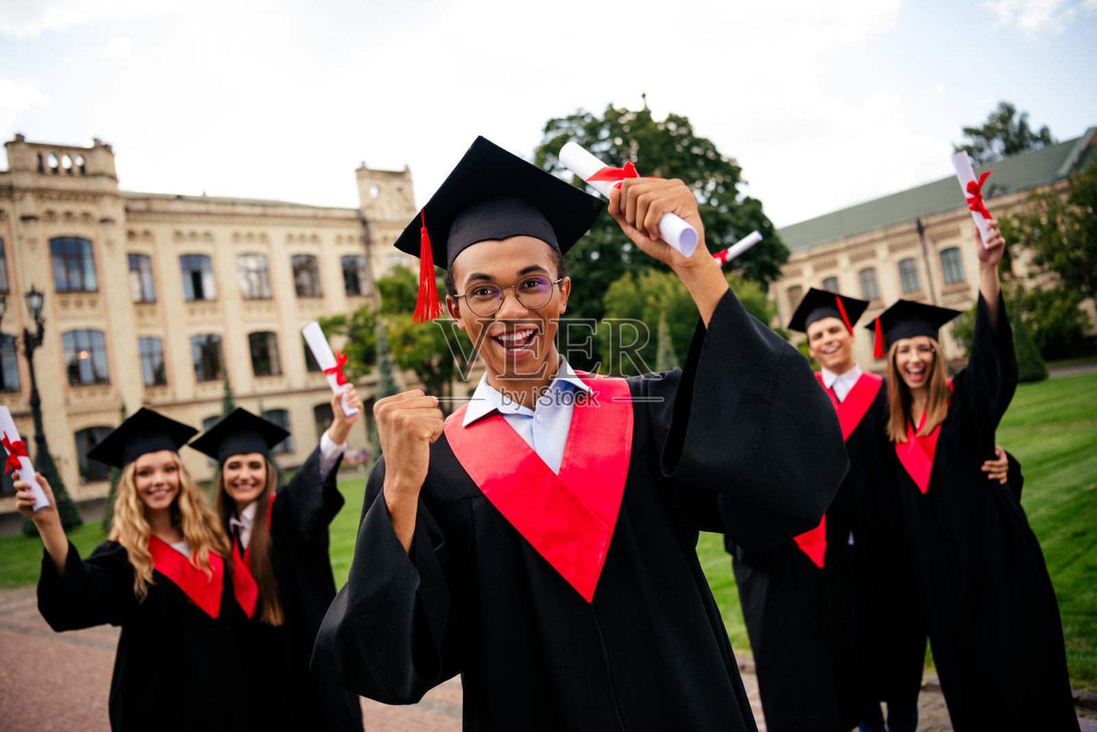 一群快乐的毕业生在阳光明媚的夏日校园外庆祝，手持文凭，身穿学士服，满怀自豪。照片摄影图片