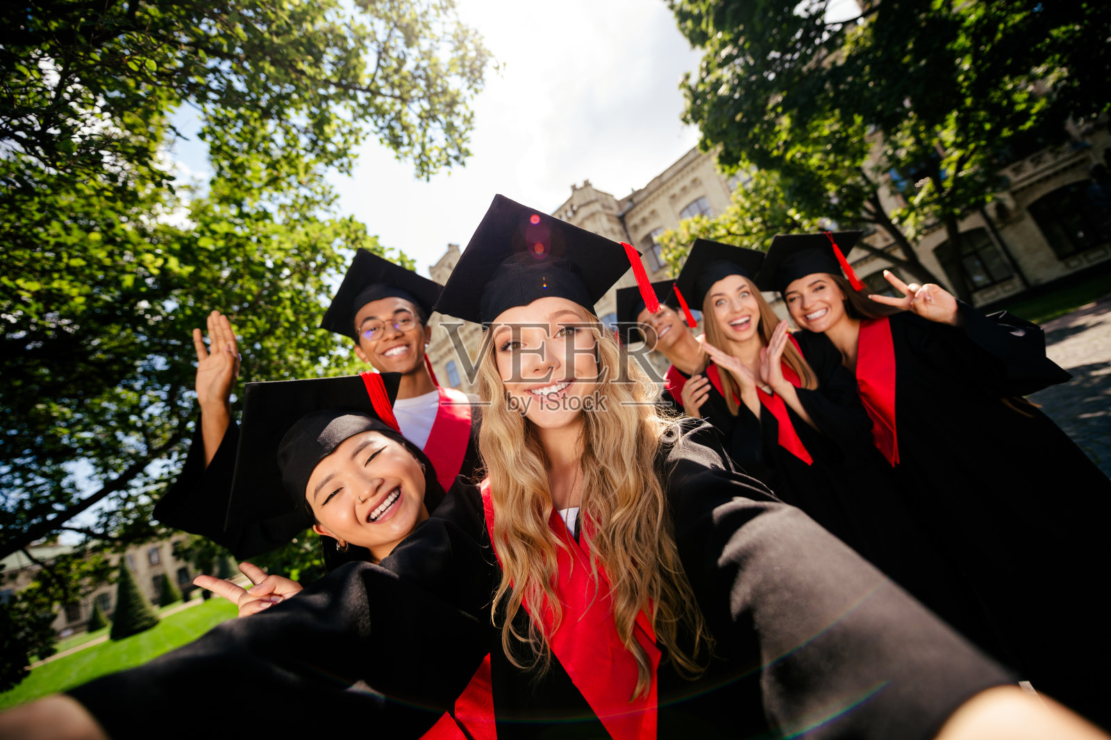 一群学生在户外大学建筑前自拍，做出V字手势，穿着学位袍和学位帽。照片摄影图片