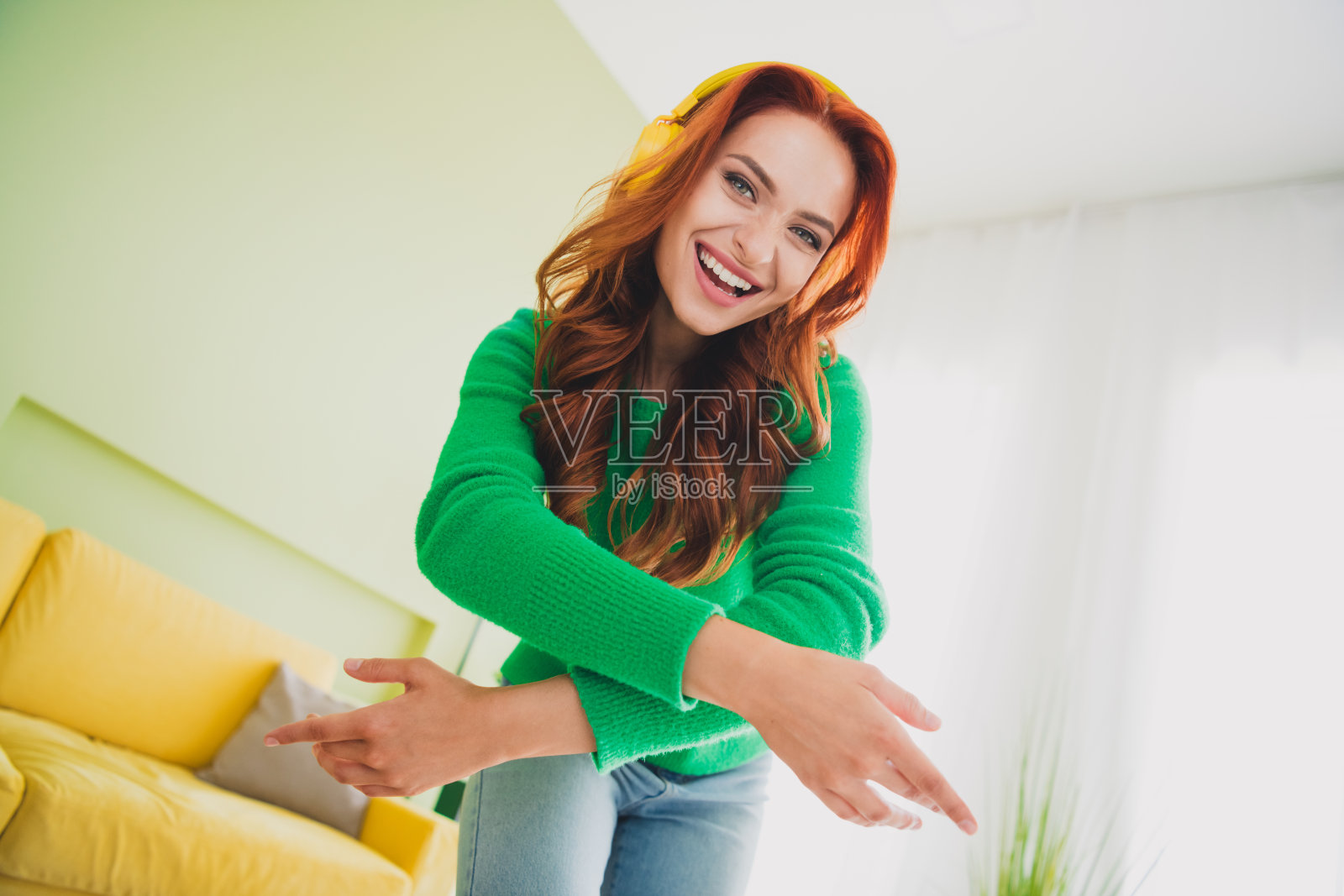 年轻女孩在现代室内公寓里穿着毛衣，戴着耳机自拍，享受周末时光。照片摄影图片