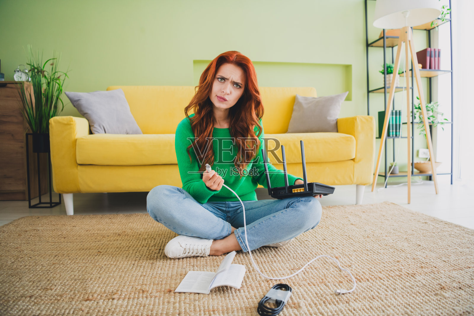 全身肖像的可爱年轻女孩手持路由器电缆，周末在现代绿色室内公寓内。照片摄影图片