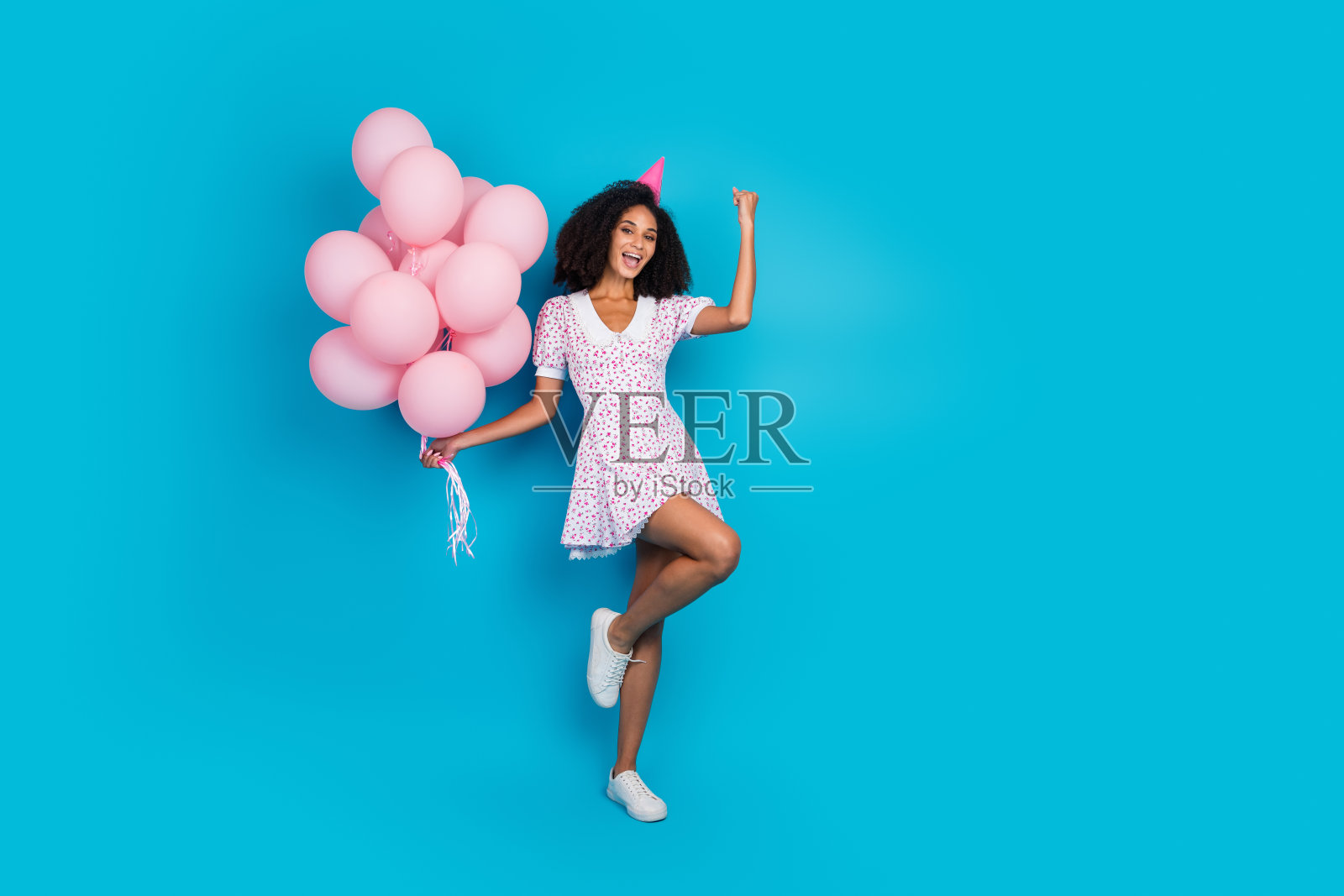 穿着时尚裙子的快乐年轻女性，手持粉色气球，在充满活力的蓝色背景下庆祝，展现出快乐与魅力。照片摄影图片
