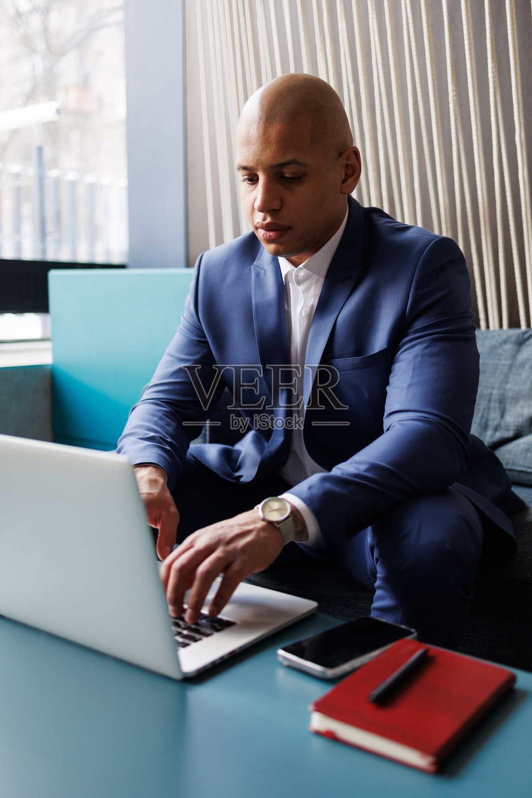 非裔美国商人在酒店大堂使用笔记本电脑，旁边放着智能手机照片摄影图片