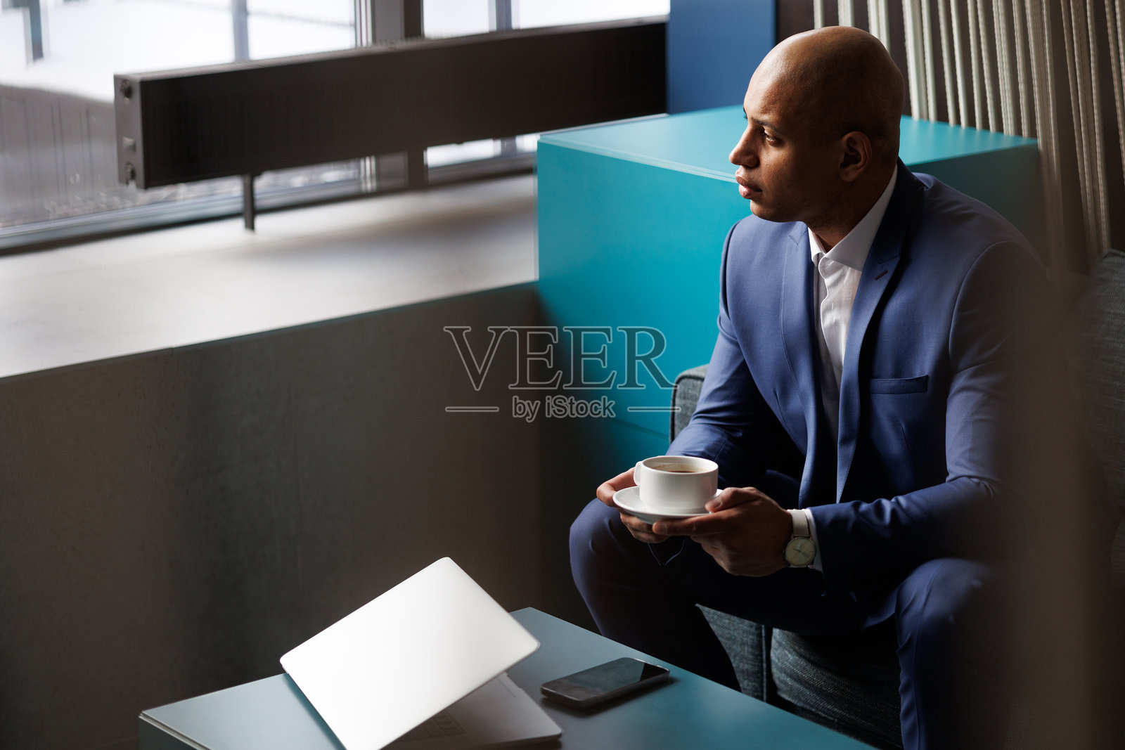 非裔美国商人在酒店里拿着咖啡，旁边有笔记本电脑和手机。照片摄影图片