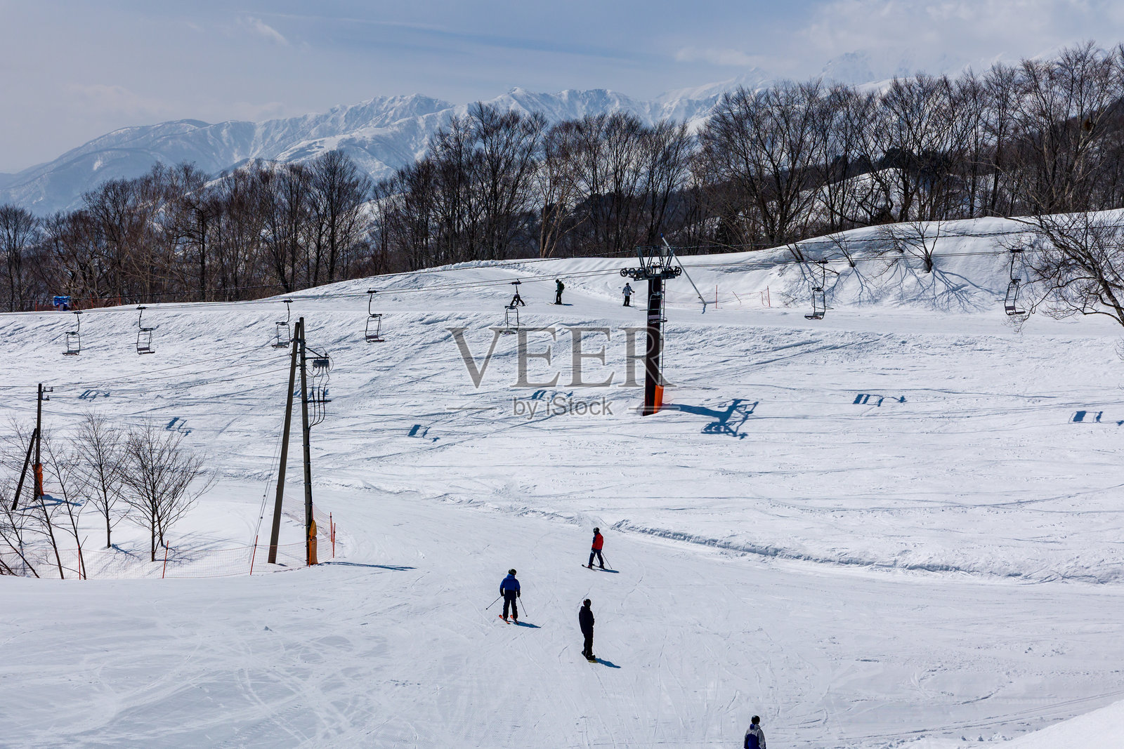 滑雪者在缆车下的狭窄坡道上，背景是山脉和树木。照片摄影图片