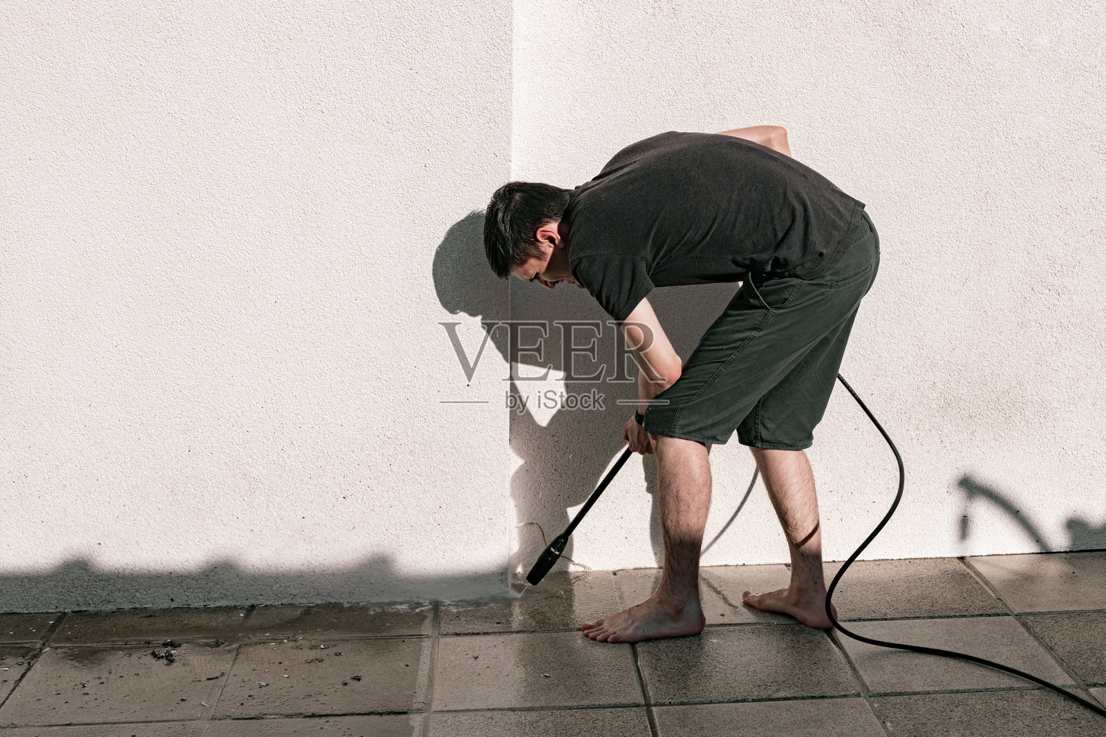 一个男孩在庭院里用高压清洗机清洗花园瓷砖。照片摄影图片