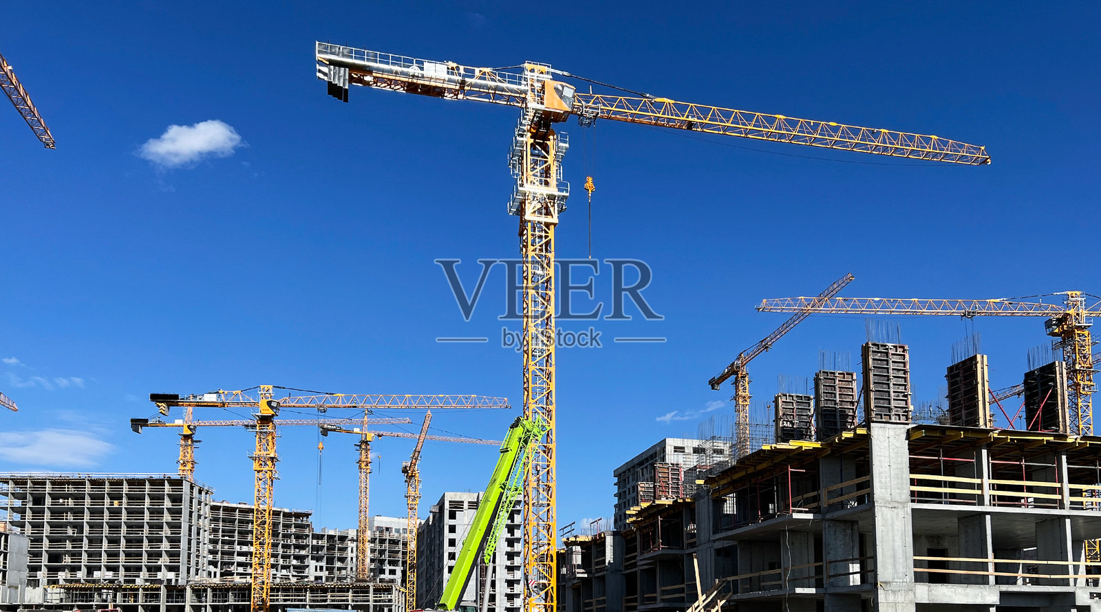 高耸的塔吊矗立在繁忙的建筑工地上，背景是晴朗的蓝天。多个建筑处于不同的施工阶段，展现现代建筑的发展。照片摄影图片