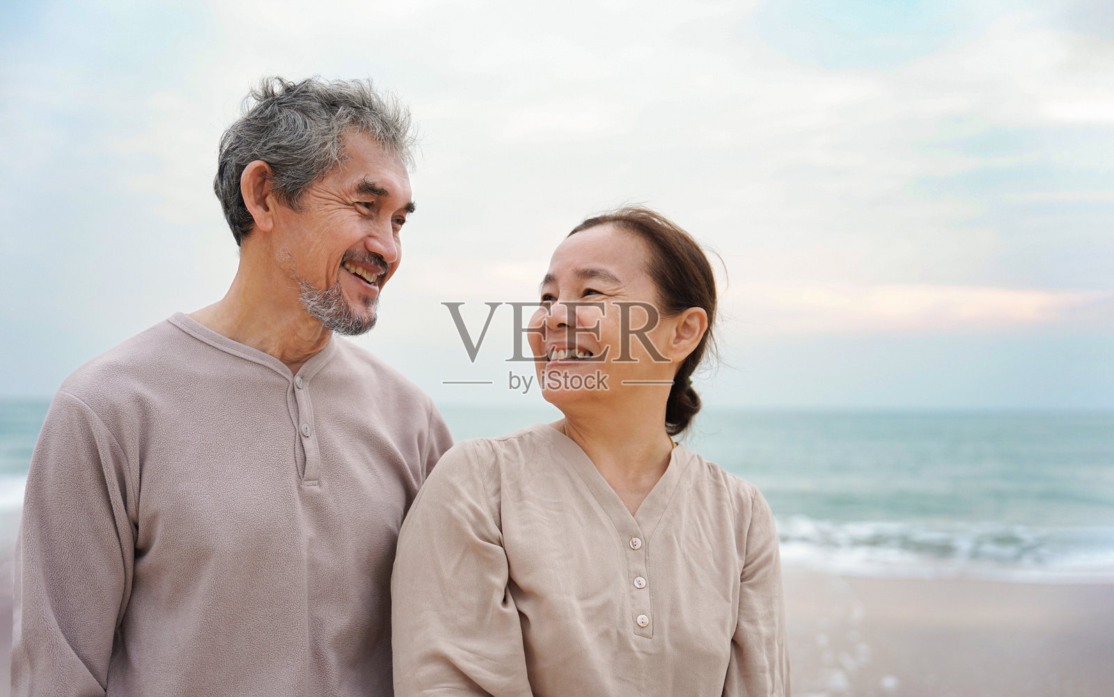 浪漫的亚洲老年夫妇在海滩上散步，微笑着，相互凝视，愉快地交谈。照片摄影图片
