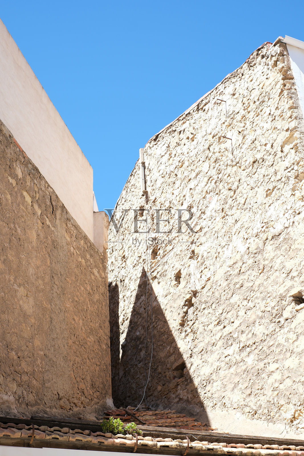 乡村风格的石墙和蓝天在阳光明媚的小巷中形成宁静的建筑对比照片摄影图片