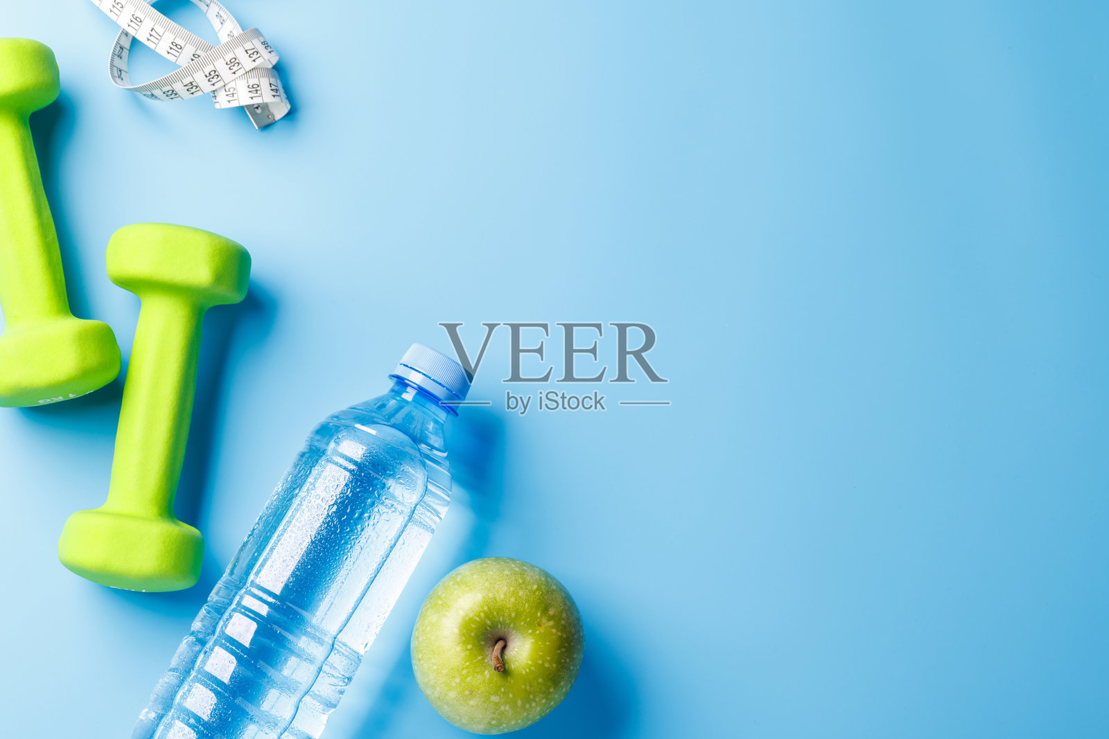 平铺的哑铃、水瓶和绿色苹果，背景为明亮的蓝色照片摄影图片