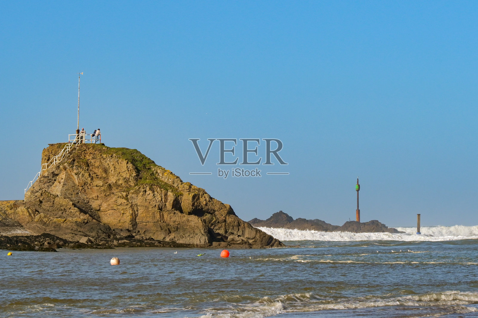 在康沃尔郡布德海滩上,一群人站在一块大岩石上照片摄影图片