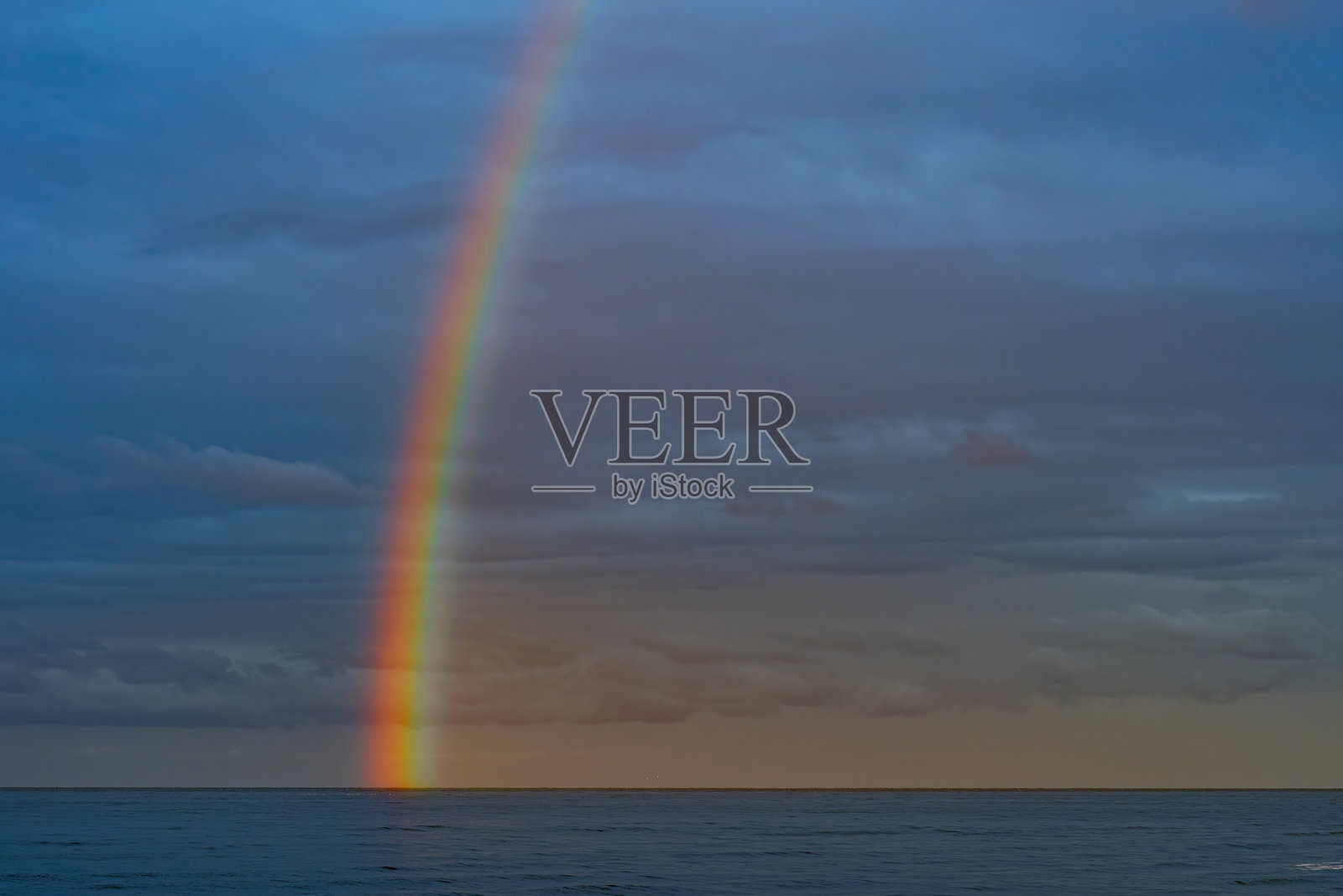 海面上阴沉天空中的闪亮彩虹。海湾上空的低云。照片摄影图片