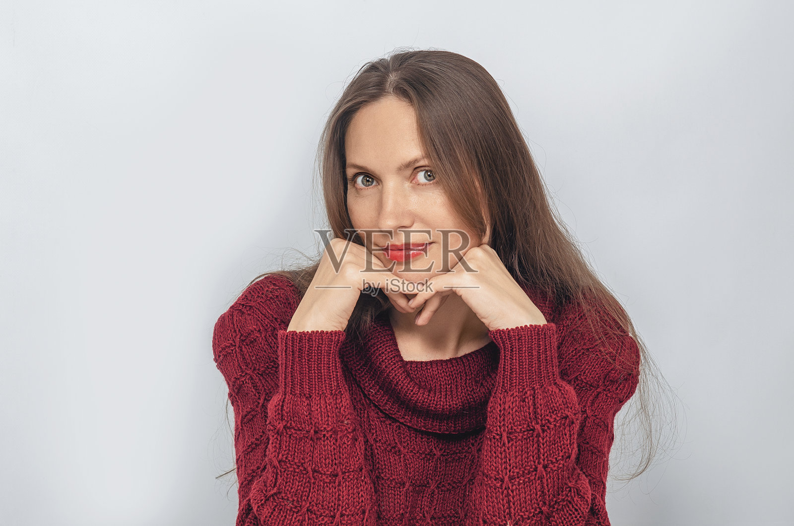穿着红色针织毛衣的女人调皮地看着，双手托着下巴，长发披肩。照片摄影图片