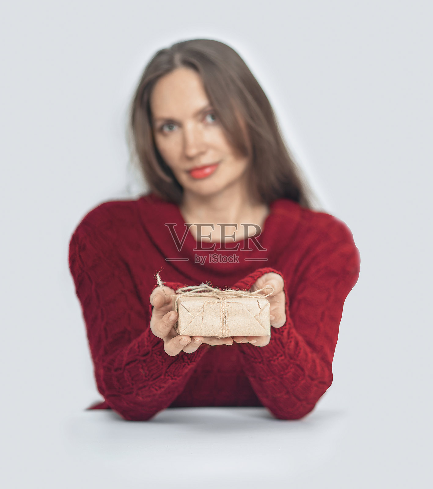 女人赠送礼物。手握着用丝带系好的牛皮纸礼盒。灰色背景。照片摄影图片