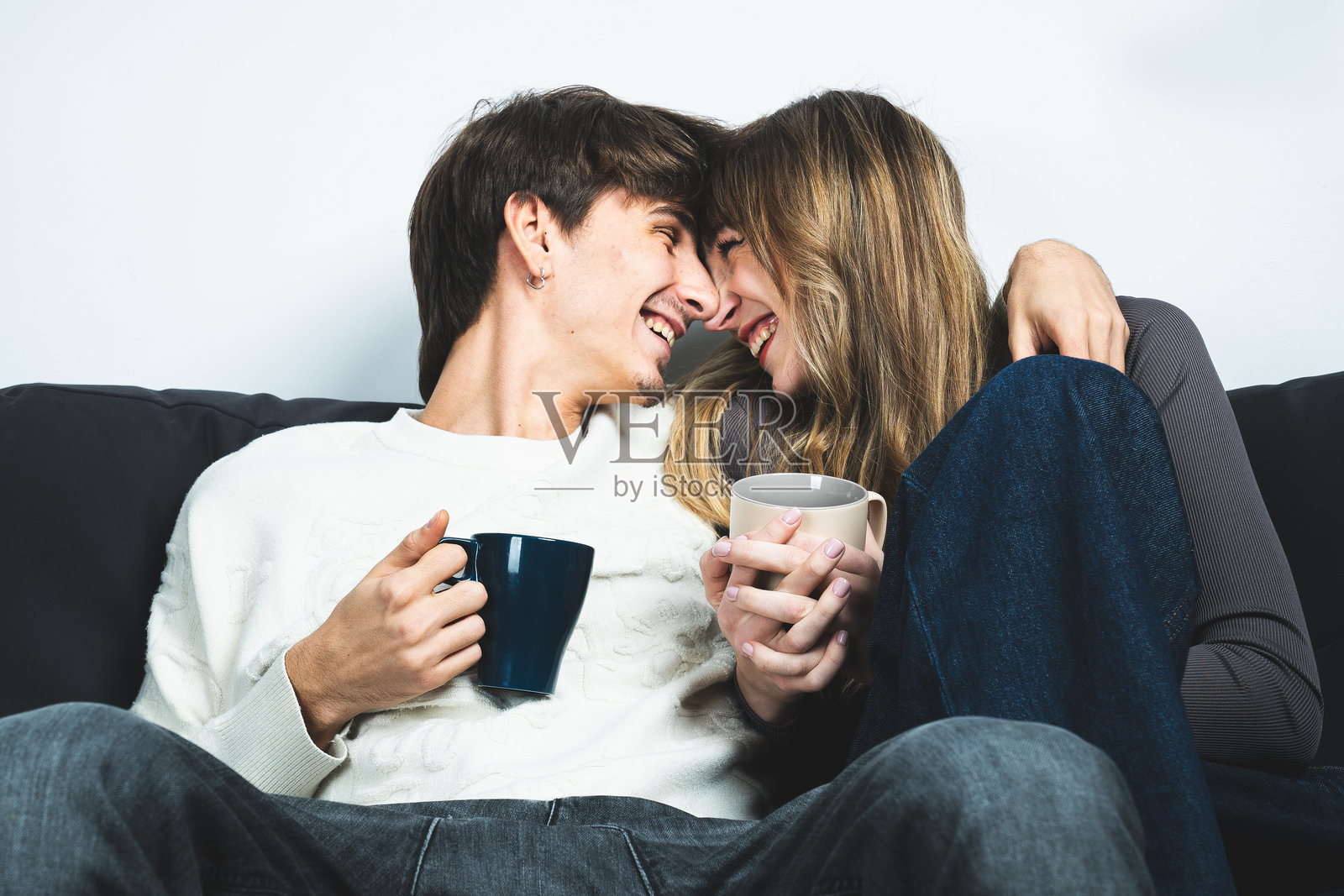 快乐的情侣在沙发上分享愉快的时刻，手里拿着咖啡杯，欢声笑语。照片摄影图片