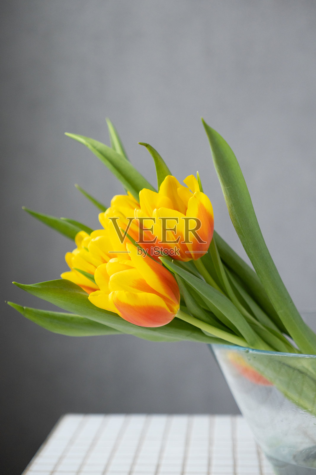 黄色郁金香与绿色叶子放在玻璃花瓶中。花艺师，花店。花束。照片摄影图片