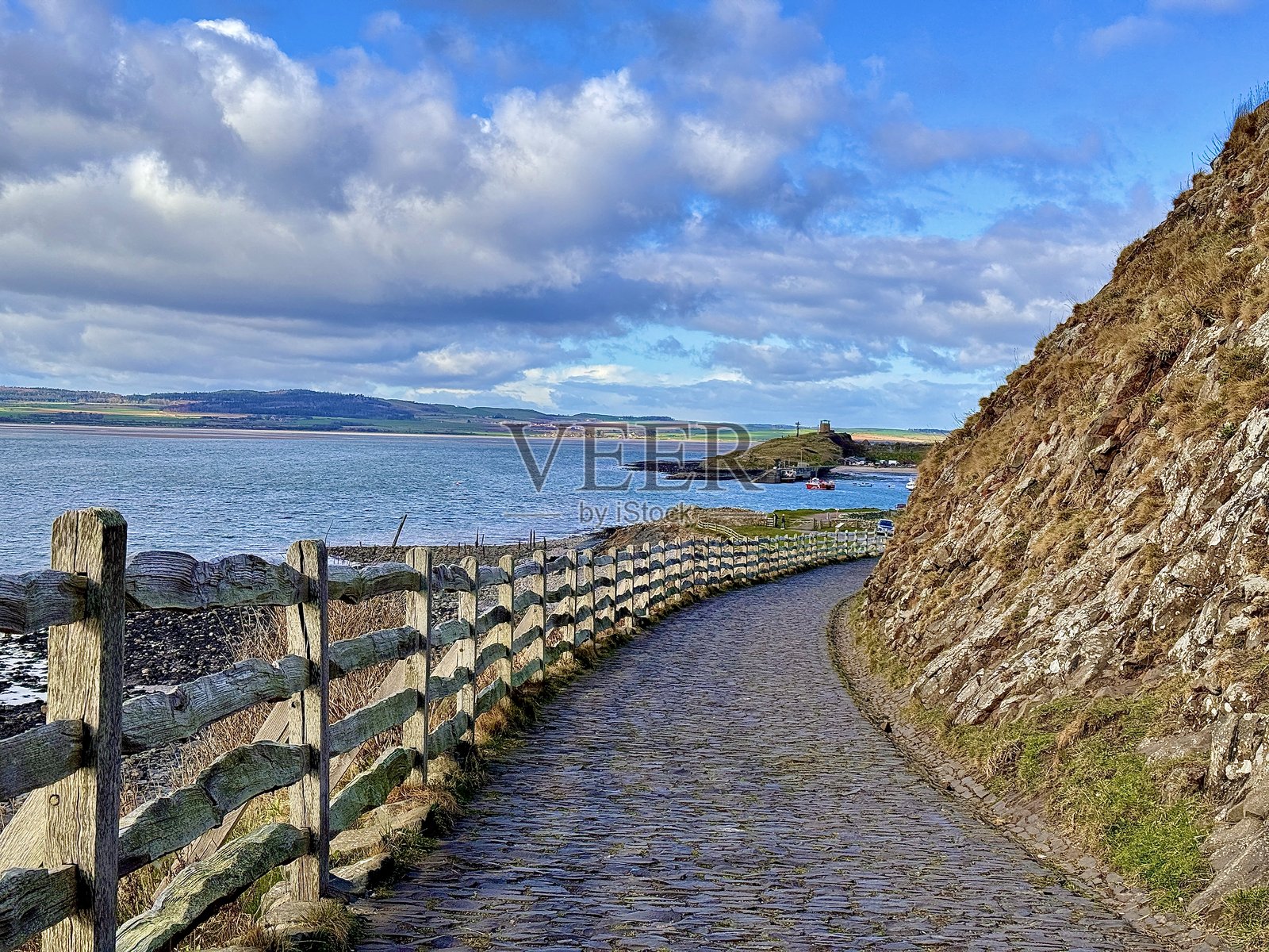 一条空旷的鹅卵石海岸小径，左侧有栅栏，背景是诺森伯兰海岸线。照片摄影图片