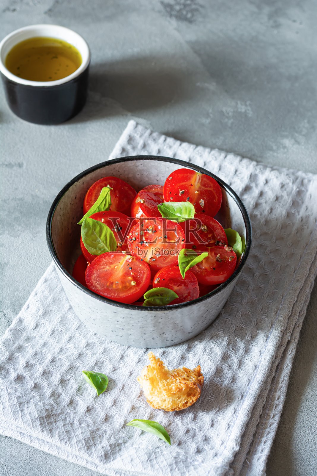 新鲜樱桃番茄沙拉，配有面包丁、罗勒叶、香料和芳香橄榄油，背景为灰色。潘扎内拉是一种在夏季受欢迎的托斯卡纳蔬菜沙拉。意大利美食。照片摄影图片
