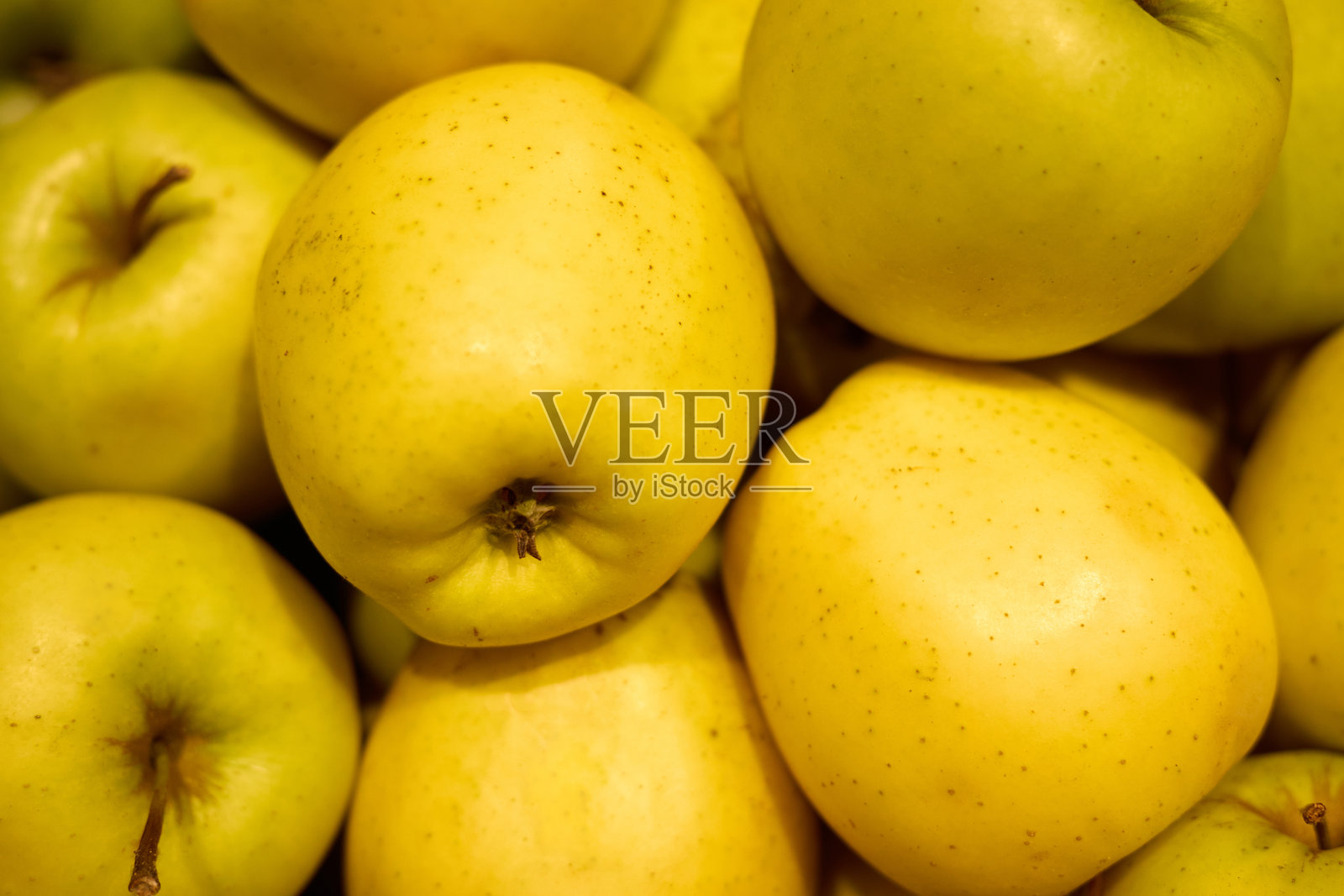 一堆新鲜的黄色苹果紧密地放在市场上。它们光滑的表皮闪闪发光，展现出诱人的颜色和新鲜感，准备出售。照片摄影图片