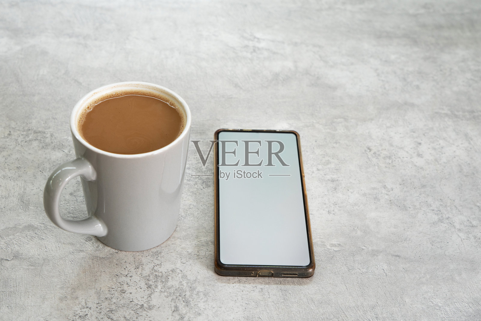 现代家居或办公室室内，一部白色空白屏幕的智能手机模型，旁边放着一杯咖啡。照片摄影图片