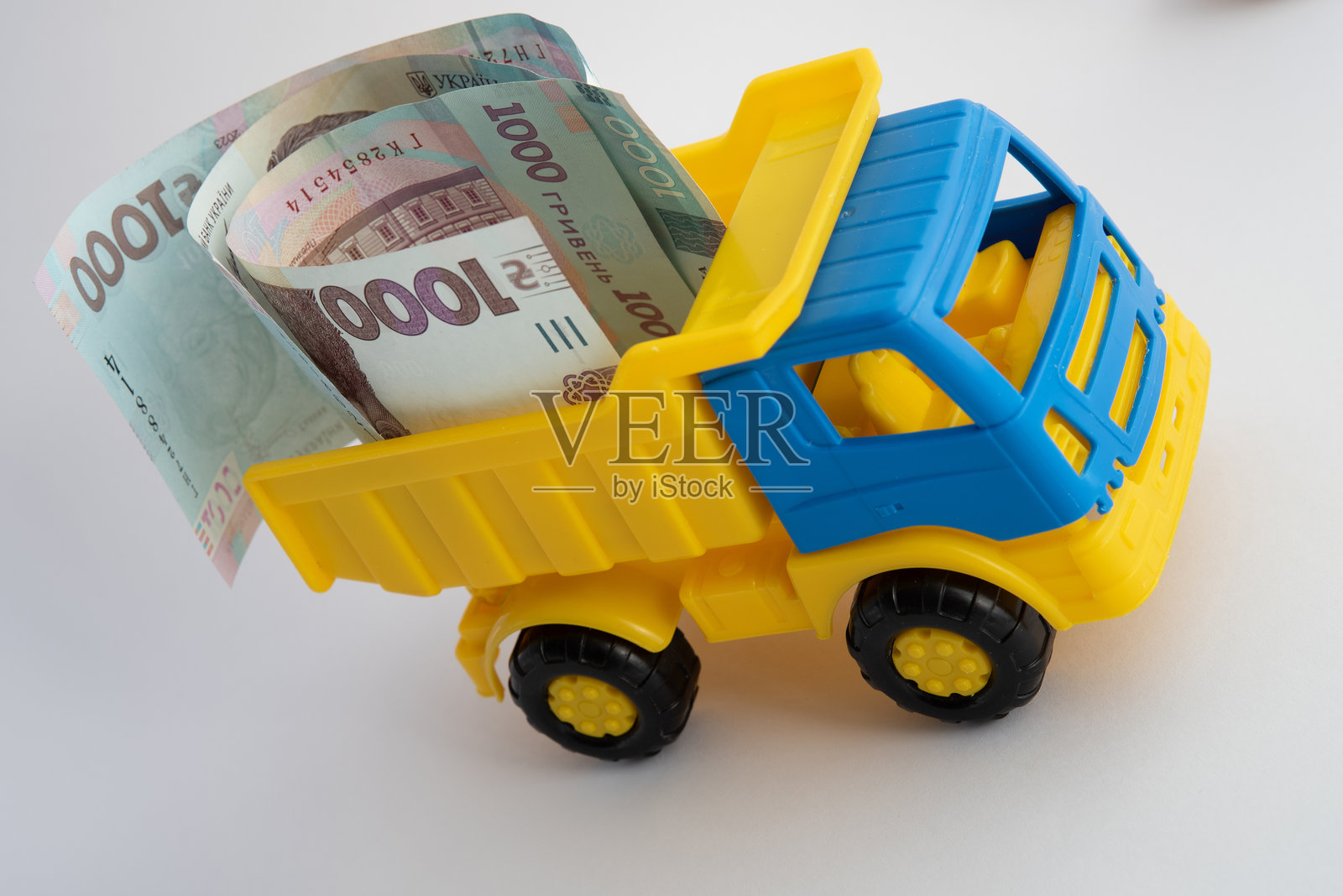现金、钱，一辆黄色和蓝色的玩具车在白色背景上载着乌克兰格里夫纳纸币。照片摄影图片