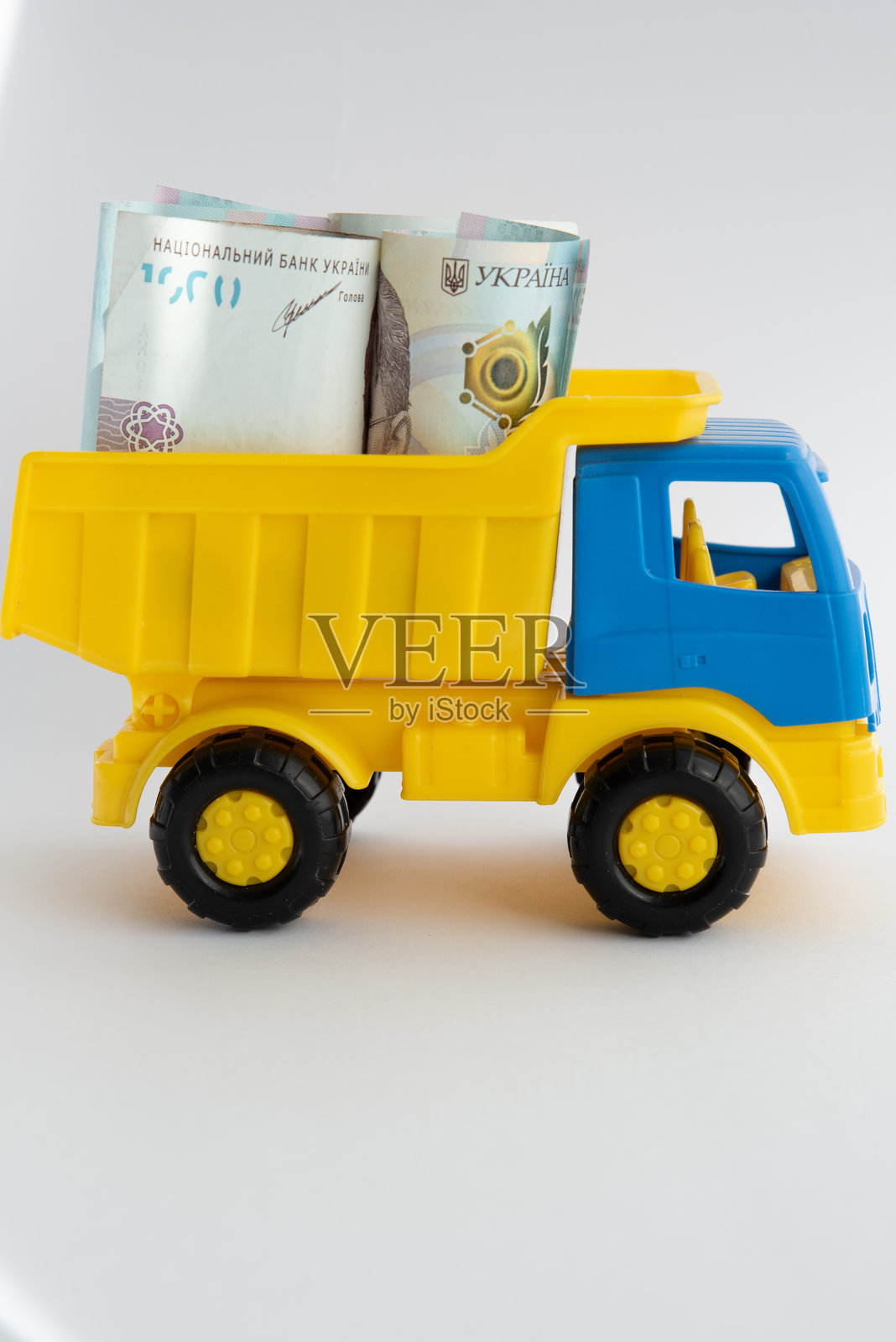 现金、钱，一辆黄色和蓝色的玩具车在白色背景上载着乌克兰格里夫纳纸币。照片摄影图片