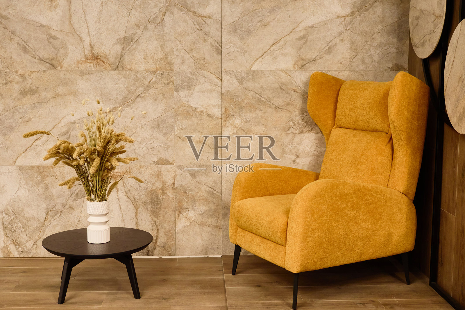 一个柔和的黄色椅子与黑色咖啡桌搭配在一个温馨宜人的角落。一个装有干花的花瓶为时尚的石墙背景增添了一丝自然气息。照片摄影图片